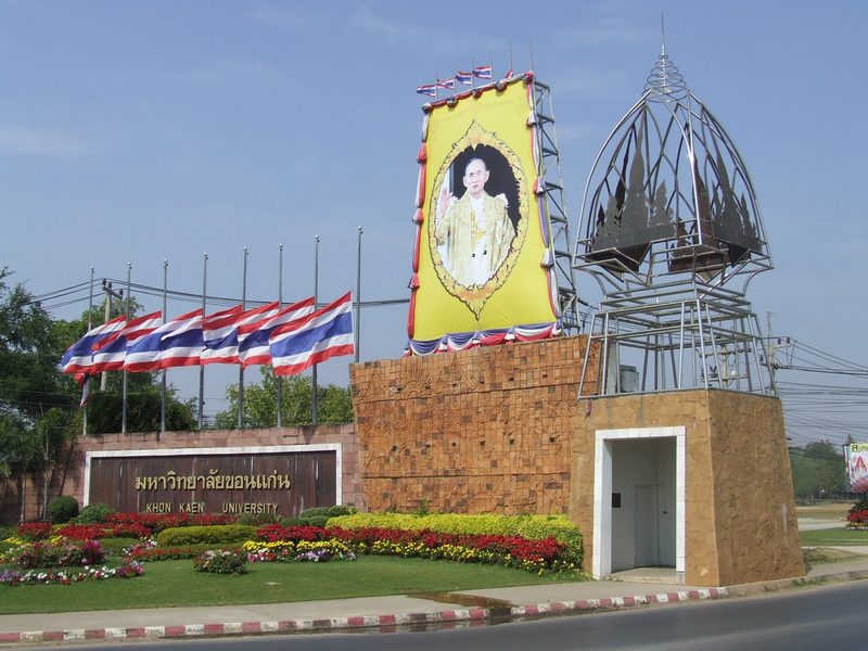 ซุ้มประตูมหาวิทยาลัยขอนแก่น มีเสาธงและสวนดอกไม้ด้านหน้า